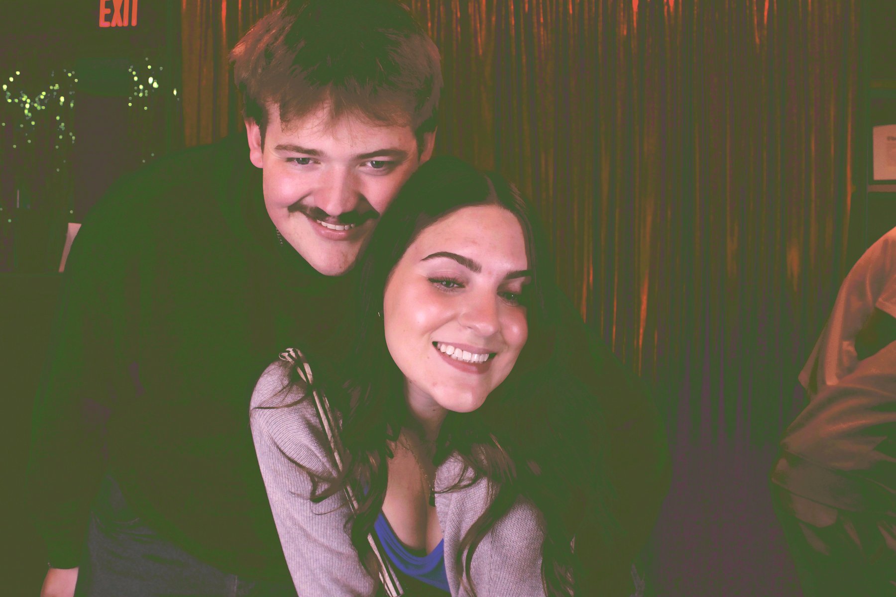 A couple leaning into the frame and laughing at the mirror photo booth during an evening event