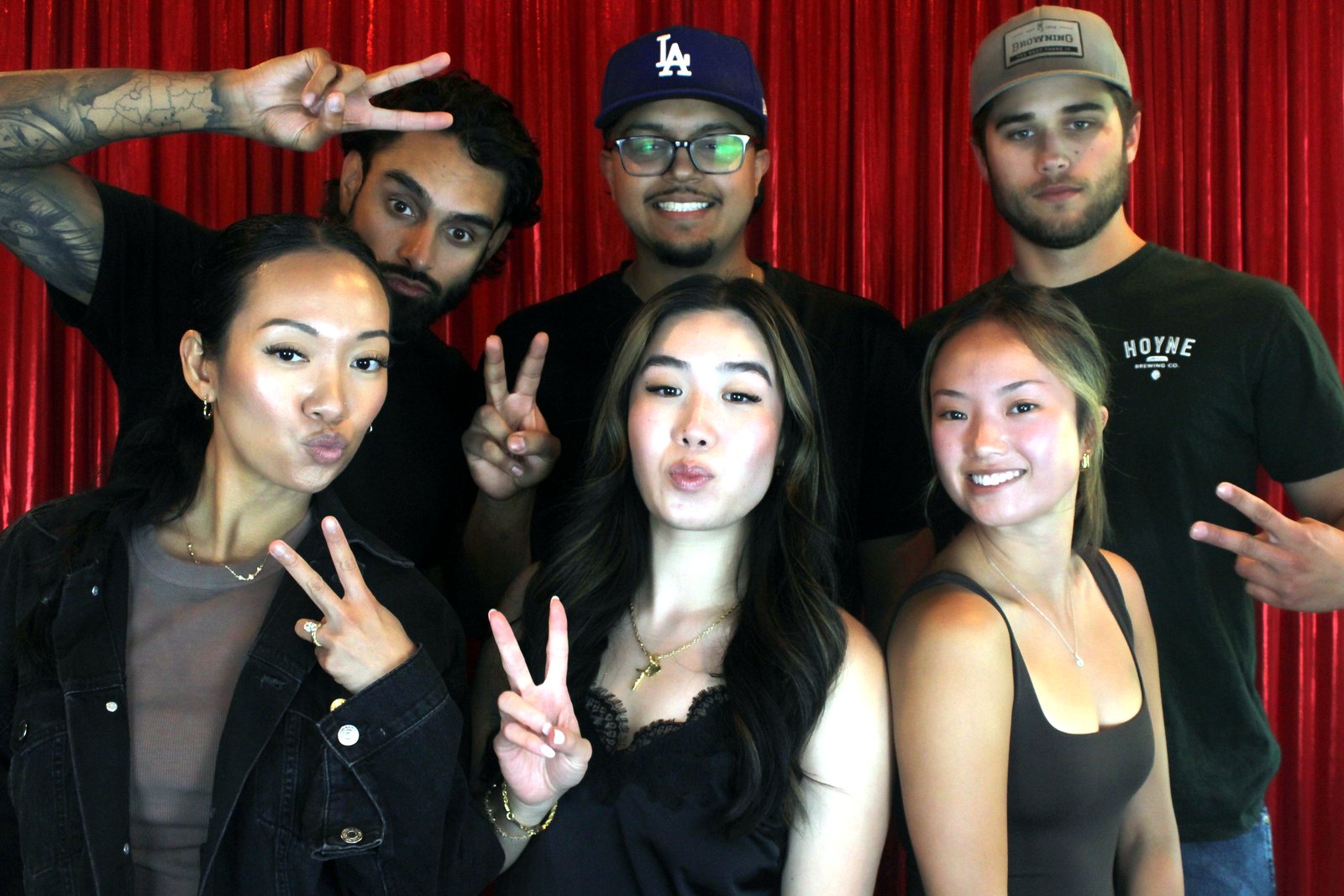 Six guests in a two-row pose, the front row of three women flashing peace signs, the back row in LA and trucker caps