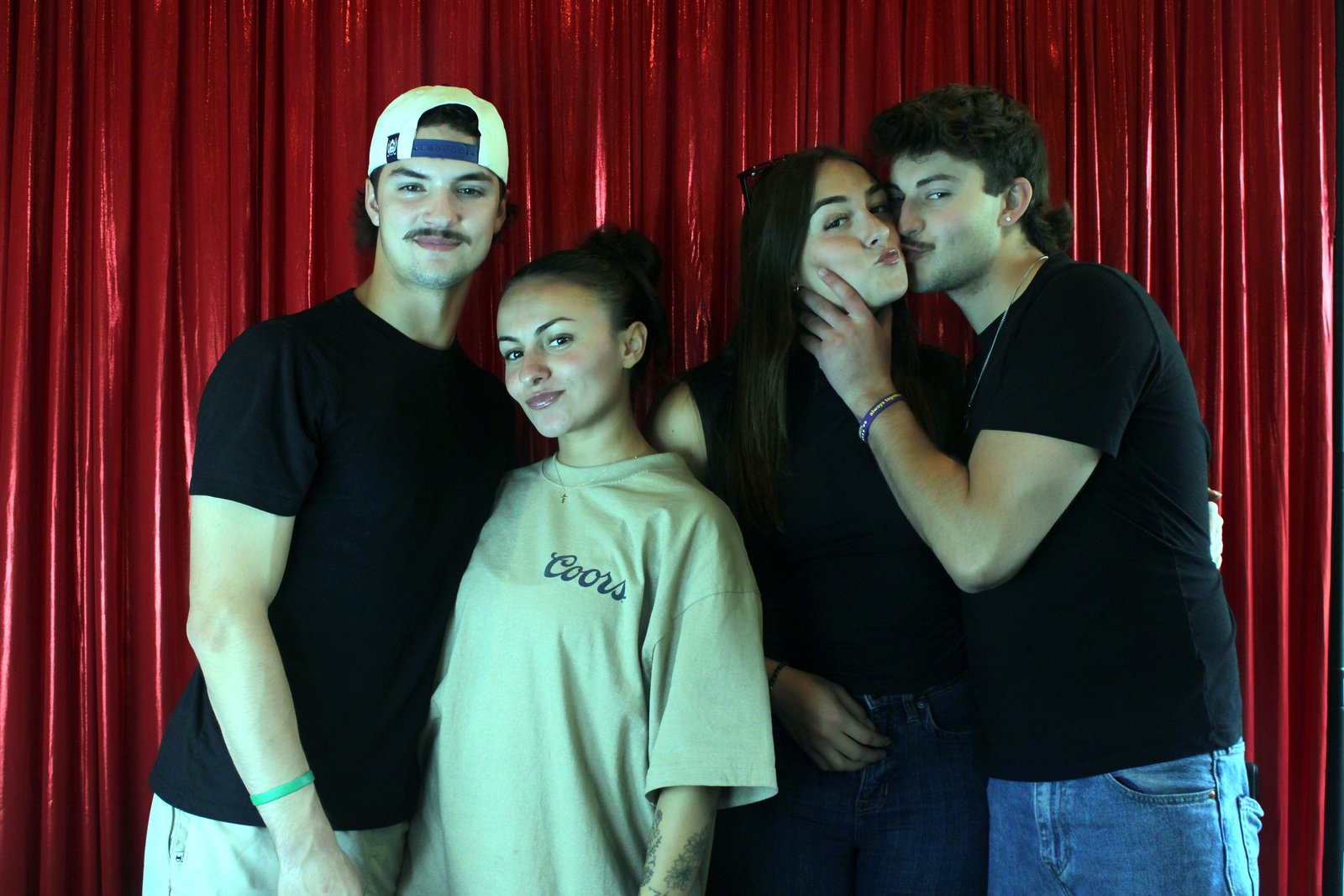 A group of four in front of the red curtain, one couple sharing a kiss on the cheek while the other two grin