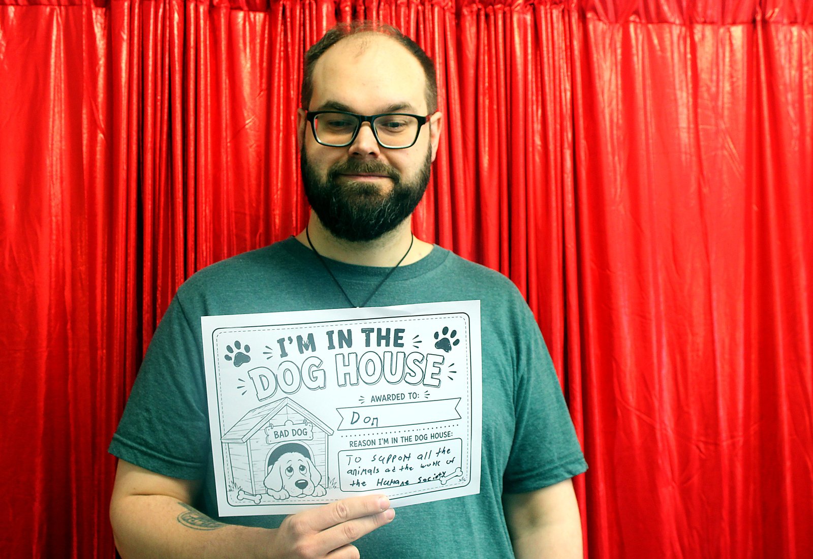 A bearded man in a green T-shirt holding an I'm in the Dog House sign