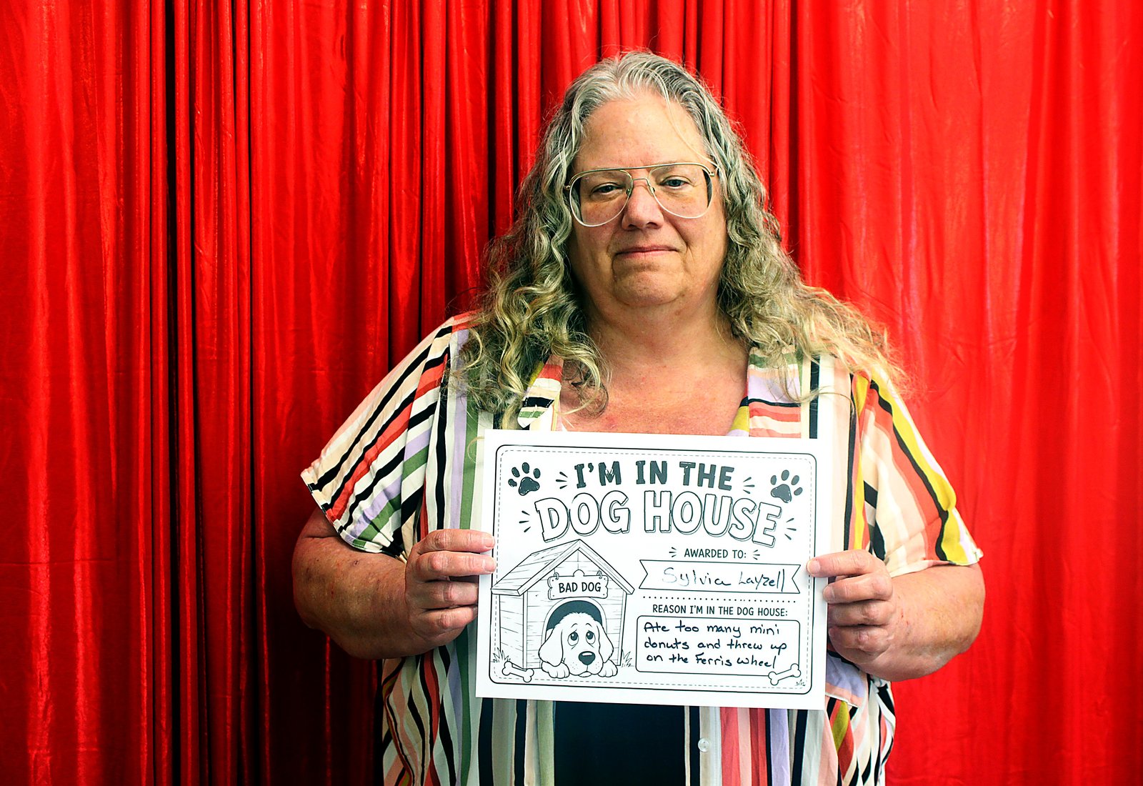 A woman with silver curls in a striped rainbow shirt holding her Dog House sign