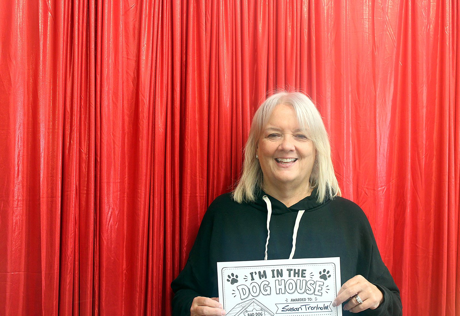 A woman with silver hair in a black hoodie smiling with her Dog House sign